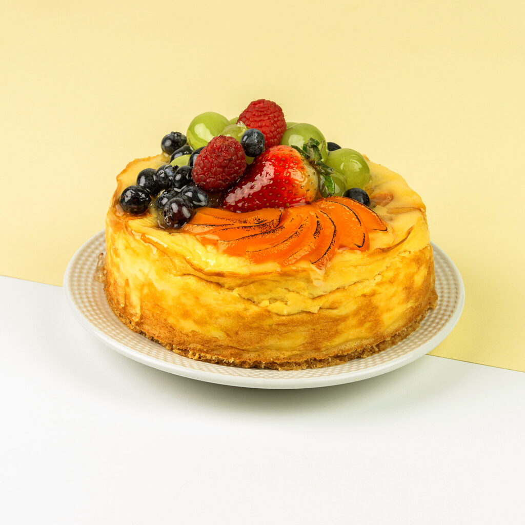 Sernik z kawałkami brzoskwiń dekorowany owocami sezonowymi
