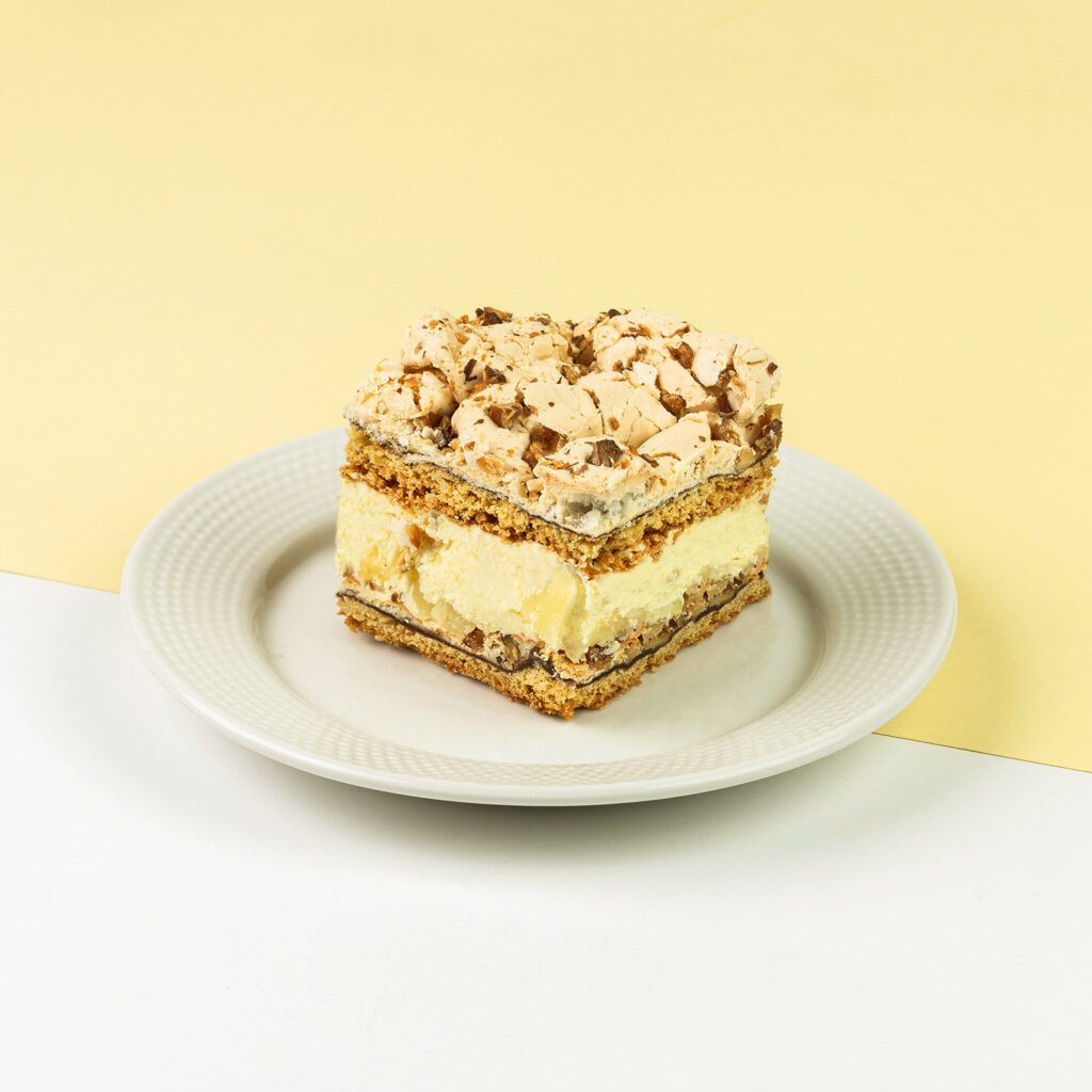 Kruche ciasto zapieczone z warstwą bezy, powidłami oraz orzechami, przełożone kremem ananasowym