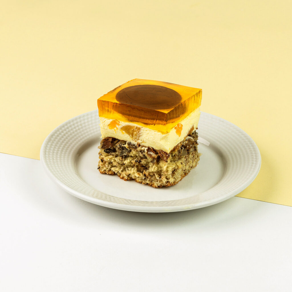 Orzechowo-kokosowy biszkopt z kremem budyniowym z brzoskwiniami wykończony galaretką brzoskwiniową i delicjami