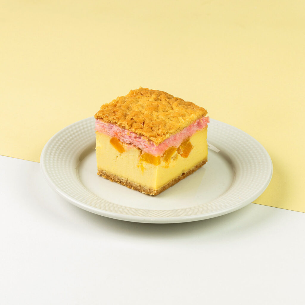 Sernik na kruchym spodzie z dodatkiem brzoskwiń pod delikatną pianką posypaną kruszonką