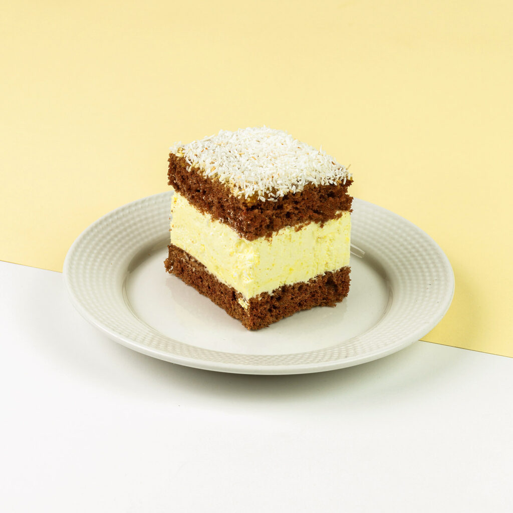 Biszkopt czekoladowy z kremem śmietankowo-serowym z rodzynkami i brzoskwiniami, dekorowany żelem morelowym i kokosem