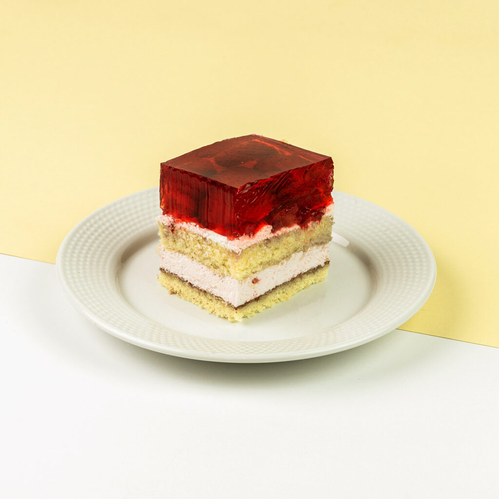 Ciasto biszkoptowe przełożone masą śmietankową, wykończone galaretką z dodatkiem truskawek