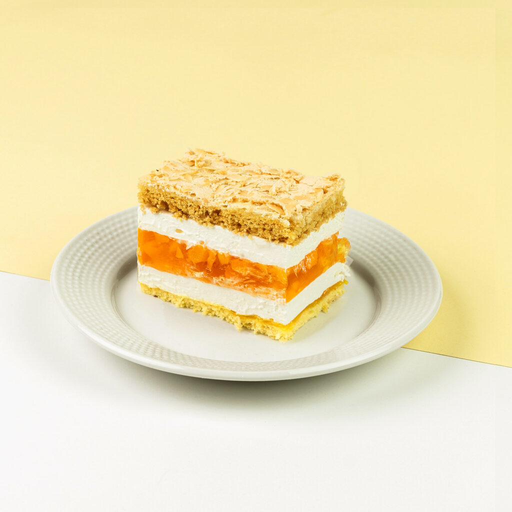 Ciasto kruche z chrupiącą bezą posypaną migdałami, z dodatkiem bitej śmietany, galaretki i dużej ilości brzoskwiń