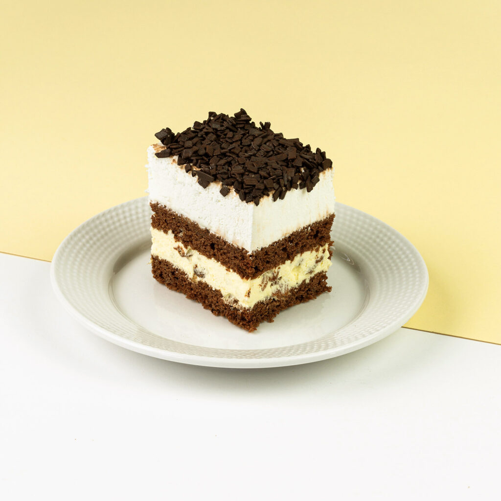 Ciasto czekoladowe przełożone delikatnym kremem budyniowym z dodatkiem rodzynek, wykończone bitą śmietaną i czekoladą