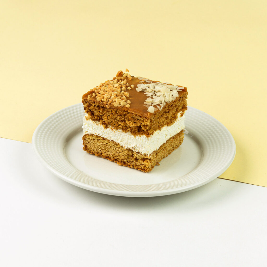 Ciasto miodowe przełożone delikatną bitą śmietaną, wykończone toffi, migdałami oraz orzechami