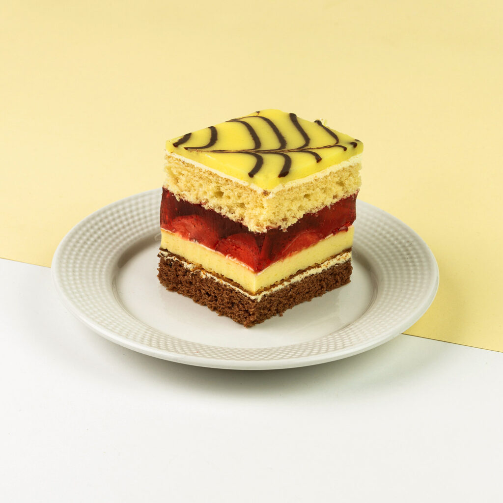 Połączenie ciasta waniliowego, czekoladowego i serowego, przełożonego kremem truskawkowym, wykończone polewą cytrynową