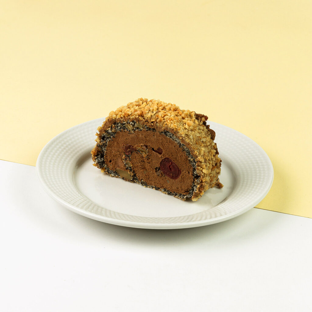 Biszkopt makowy, połączony z puszystym kremem czekoladowym z dodatkiem wiśni, wykończony orzechami