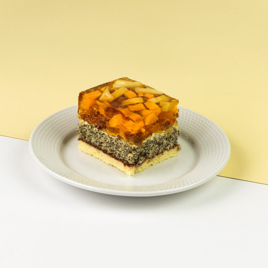 Jasny biszkopt, powidło śliwkowe, wkładka makowa, całość zwieńczona rodzynkami, ananasami i brzoskwiniami zalanymi galaretką brzoskwiniową