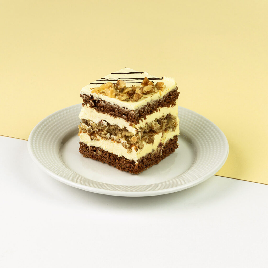 Biszkopt czekoladowy oraz orzechowy połączony z delikatnym kremem budyniowym, wykończony czekoladą i orzechami