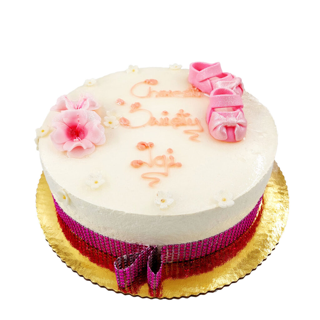 Tort na z jasnoróżowym napisem Chrzest Święty Igi ozdobiony różowymi kwiatkami oraz małymi butkami dla dziewczynki.