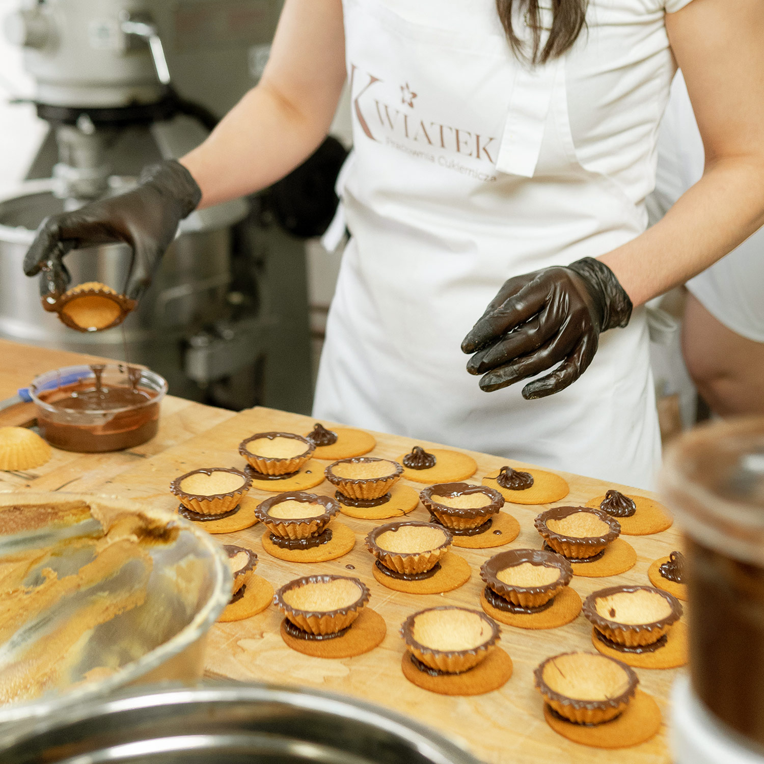 Pracownik Cukierni Kwiatek przygotowujący ciasteczka babeczki z polewą czekoladową.