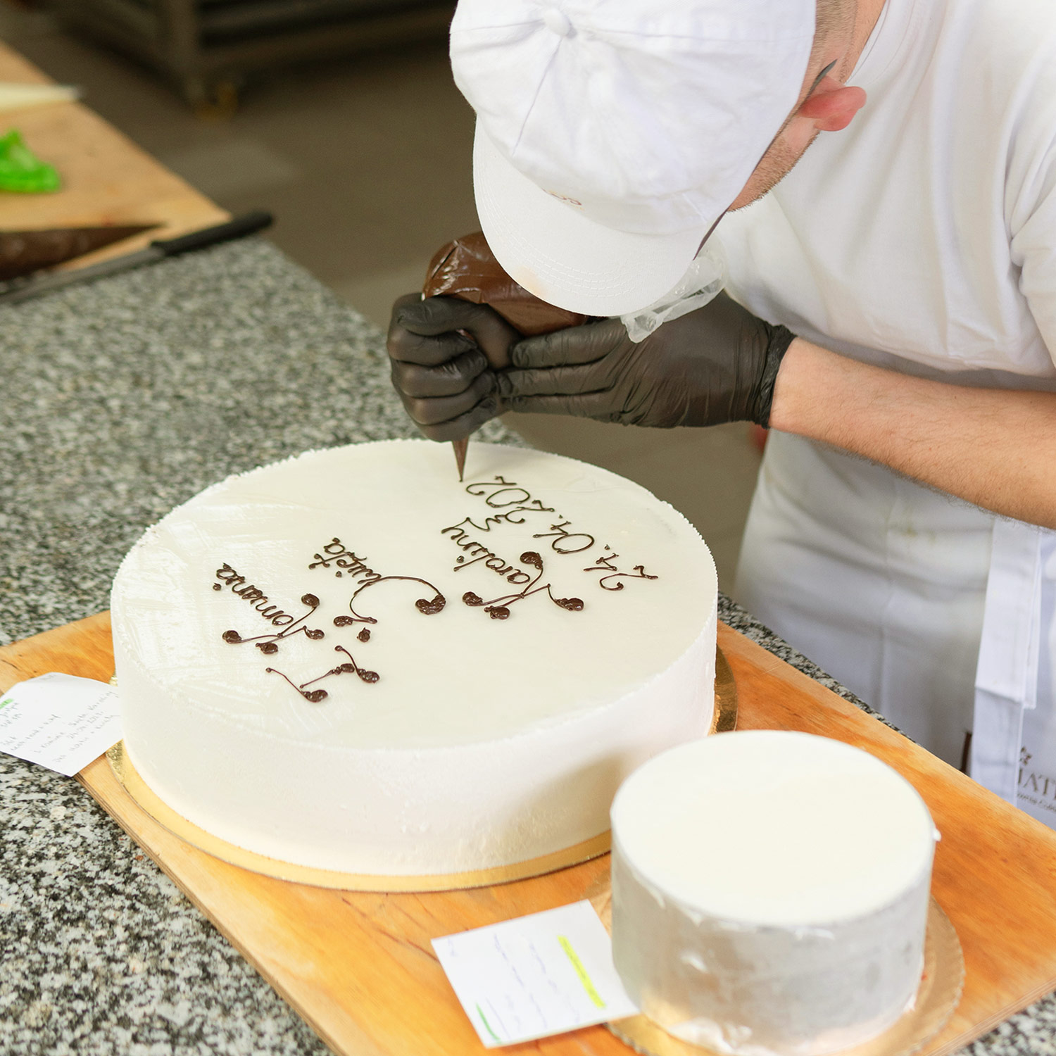 Pracownik Cukierni Kwiatek przygotowujący i podpisujący tort czekoladową polewą.