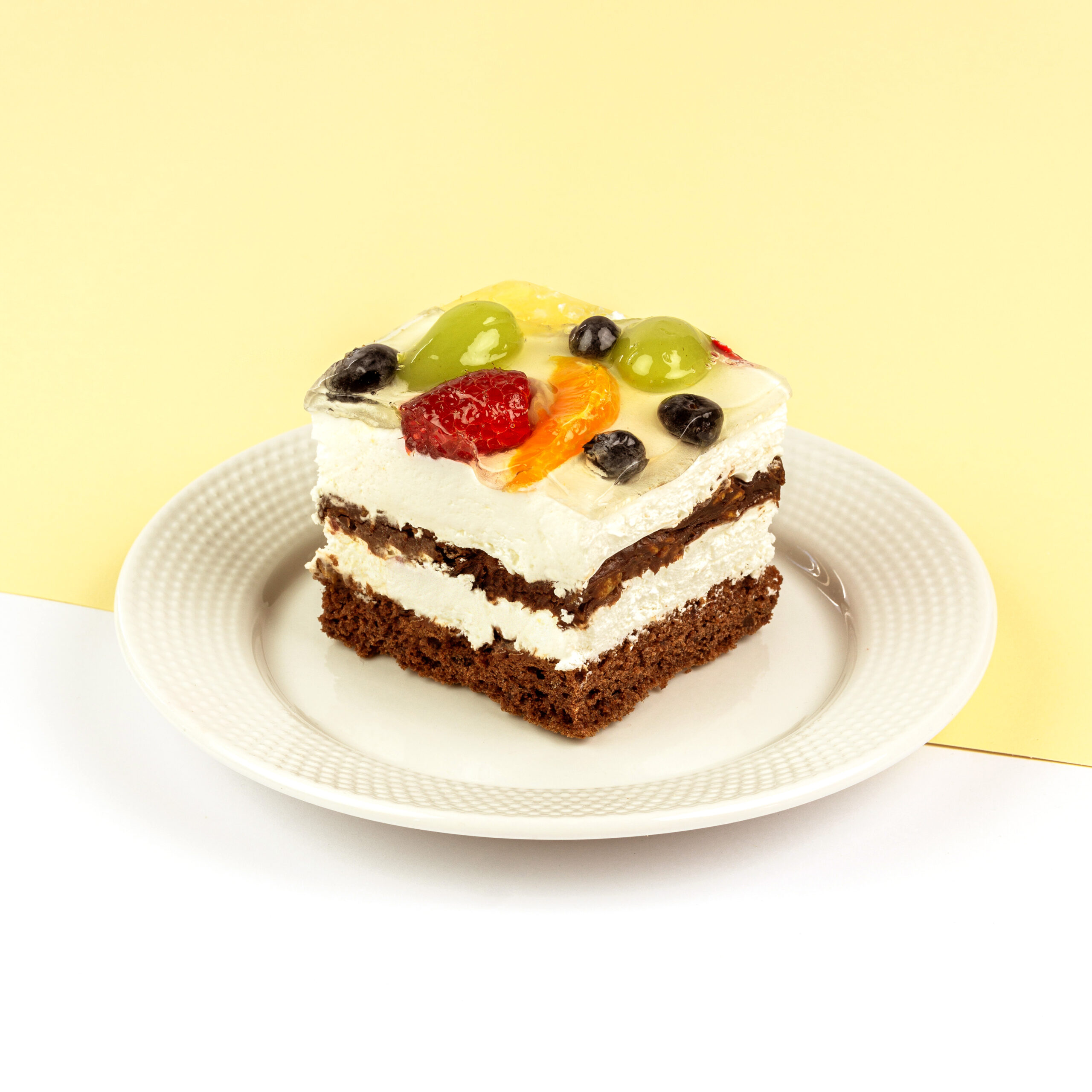 Czekoladowe biszkopty przełożone bitą śmietaną, całość dekorowana owocami w żelu