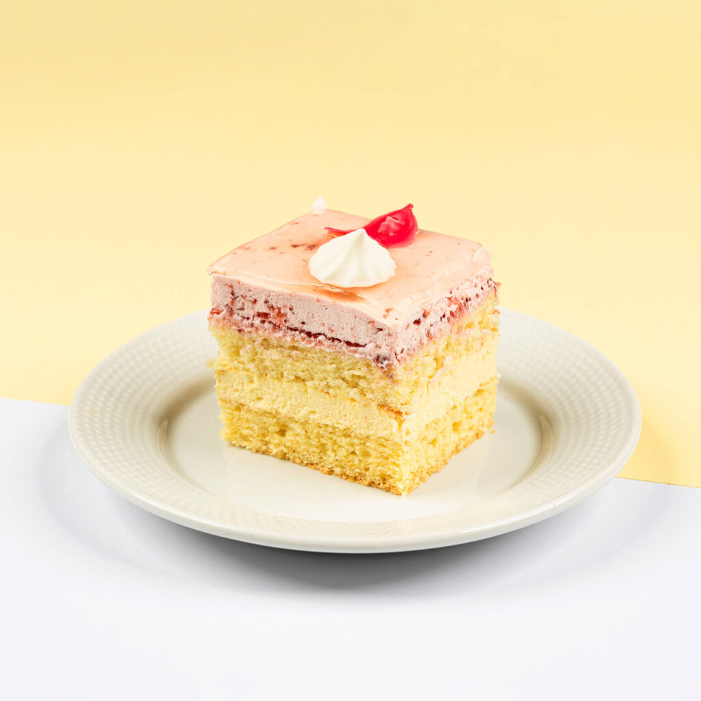 Śmietankowe biszkopty przełożone kremem budyniowym, wykończone warstwą musu truskawkowego oraz śmietany o smaku truskawkowym. Całość dekorowana kleksami ze śmietany oraz czekoladowymi płatkami