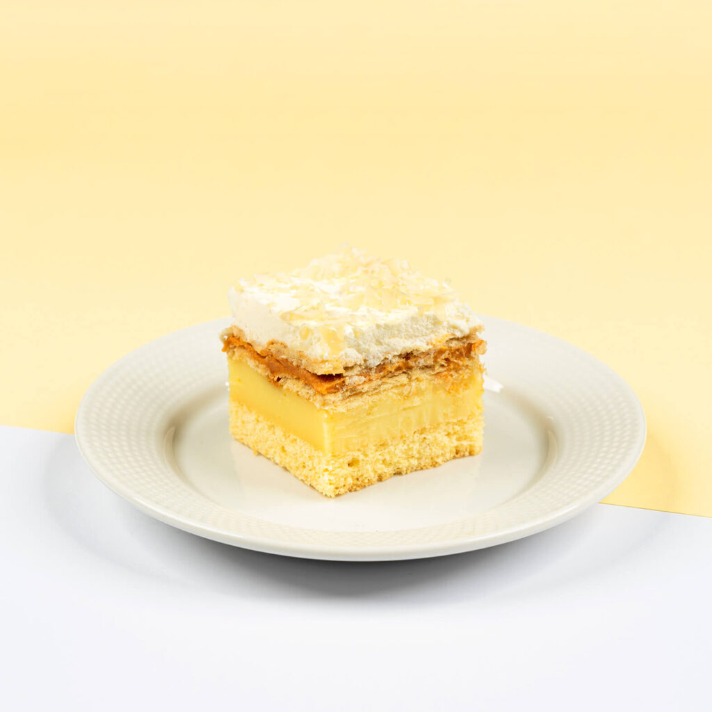 Delikatny biszkopt przełożony kremem budyniowym, krakersami oraz toffi, wykończony bitą śmietaną oraz migdałami