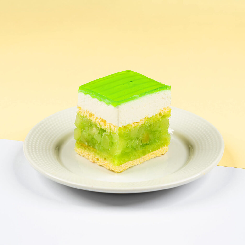 Ciasto biszkoptowe przełożone warstwą jabłek oraz bitą śmietaną, wykończone soczyście zieloną galaretką